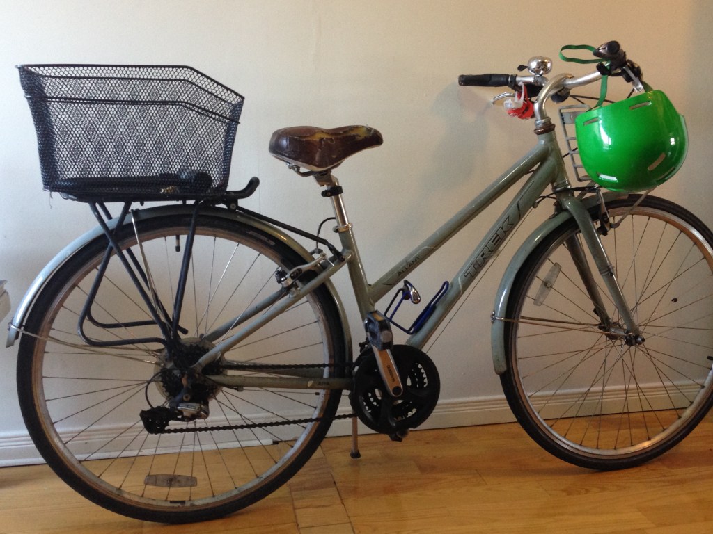 A light green bicycle with carrier basket at the back, a green helmet hanging on handle bar